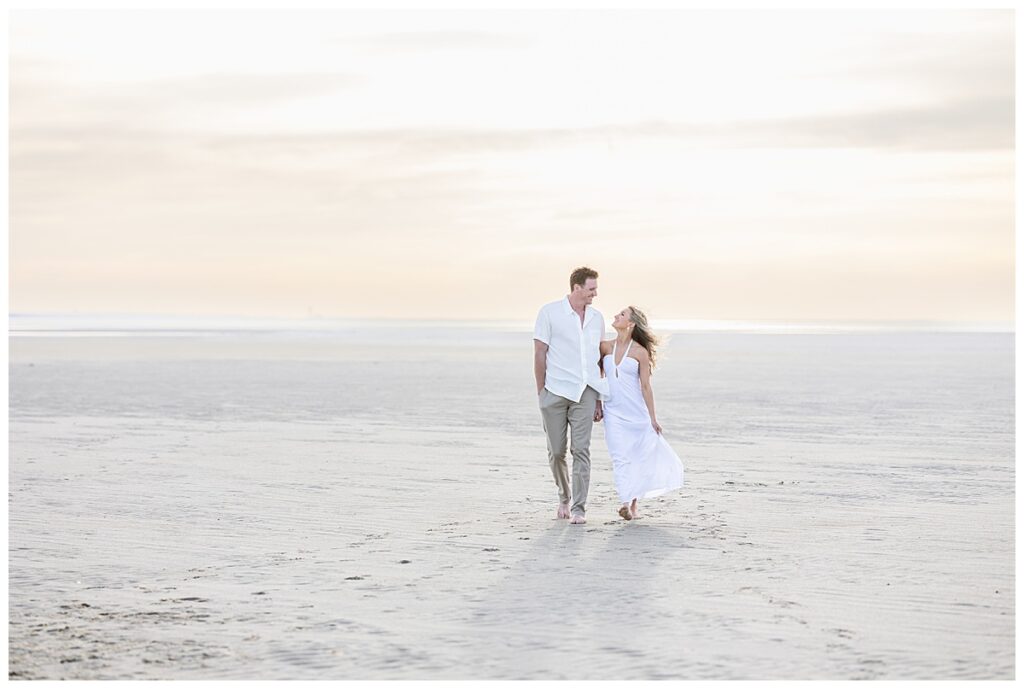 Couple walk along Chapin beach in Cape Cod. Newly engaged, the girl is wearing a white dress.