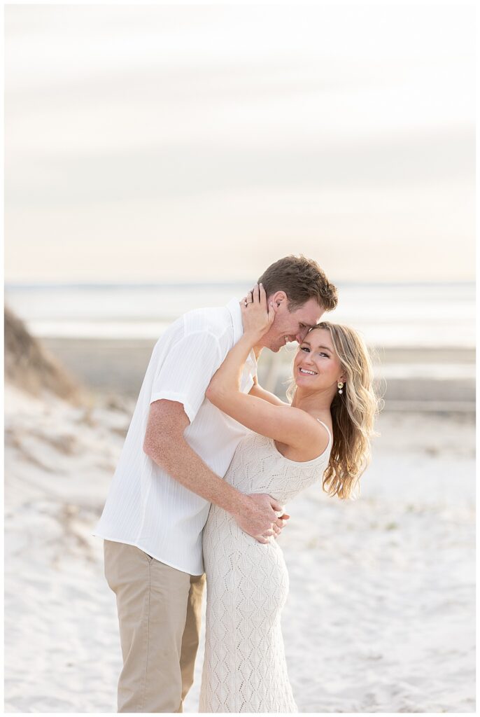 Engaged couple hug and embrace next to the dunes in Cape Cod at Chapin Memorial Beach during sunset.