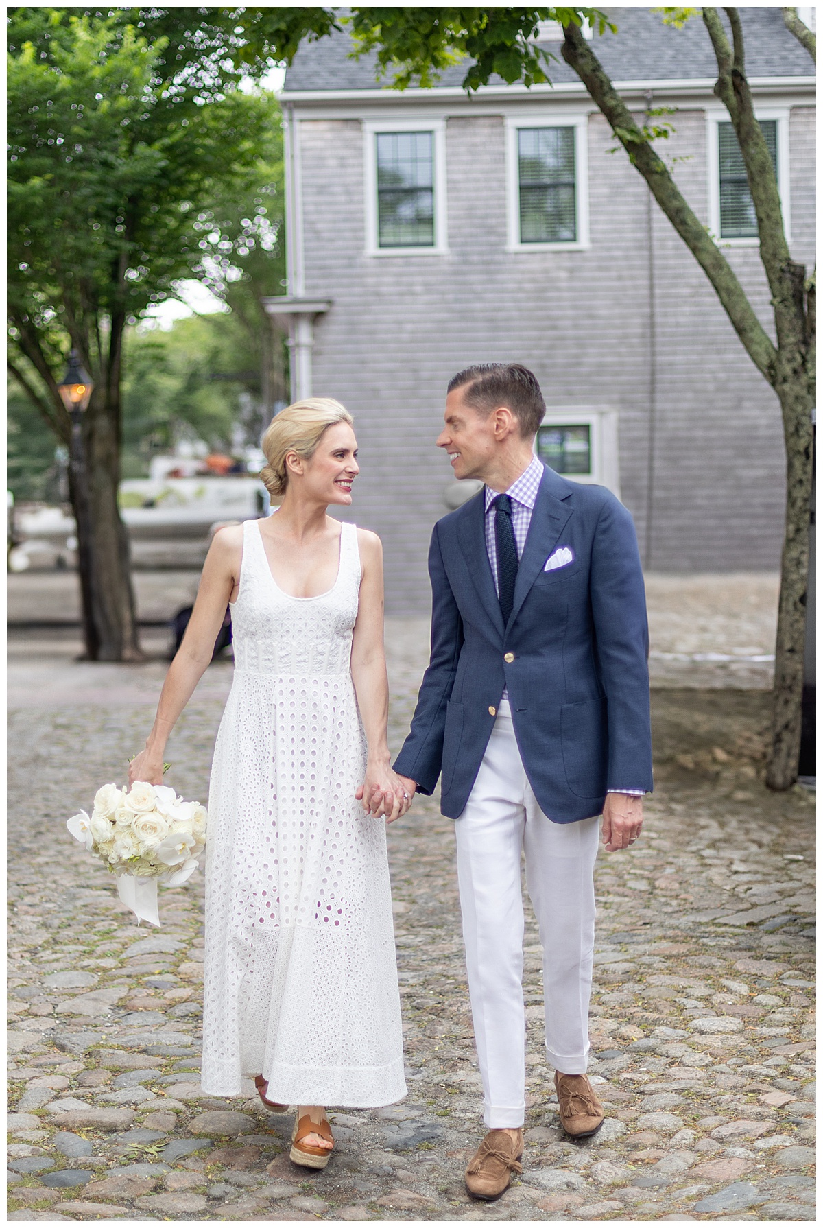 Bride and groom in Nantucket walking holding hands by the Old North Wharf. Bride wearing white dress groom in loafers and suit.