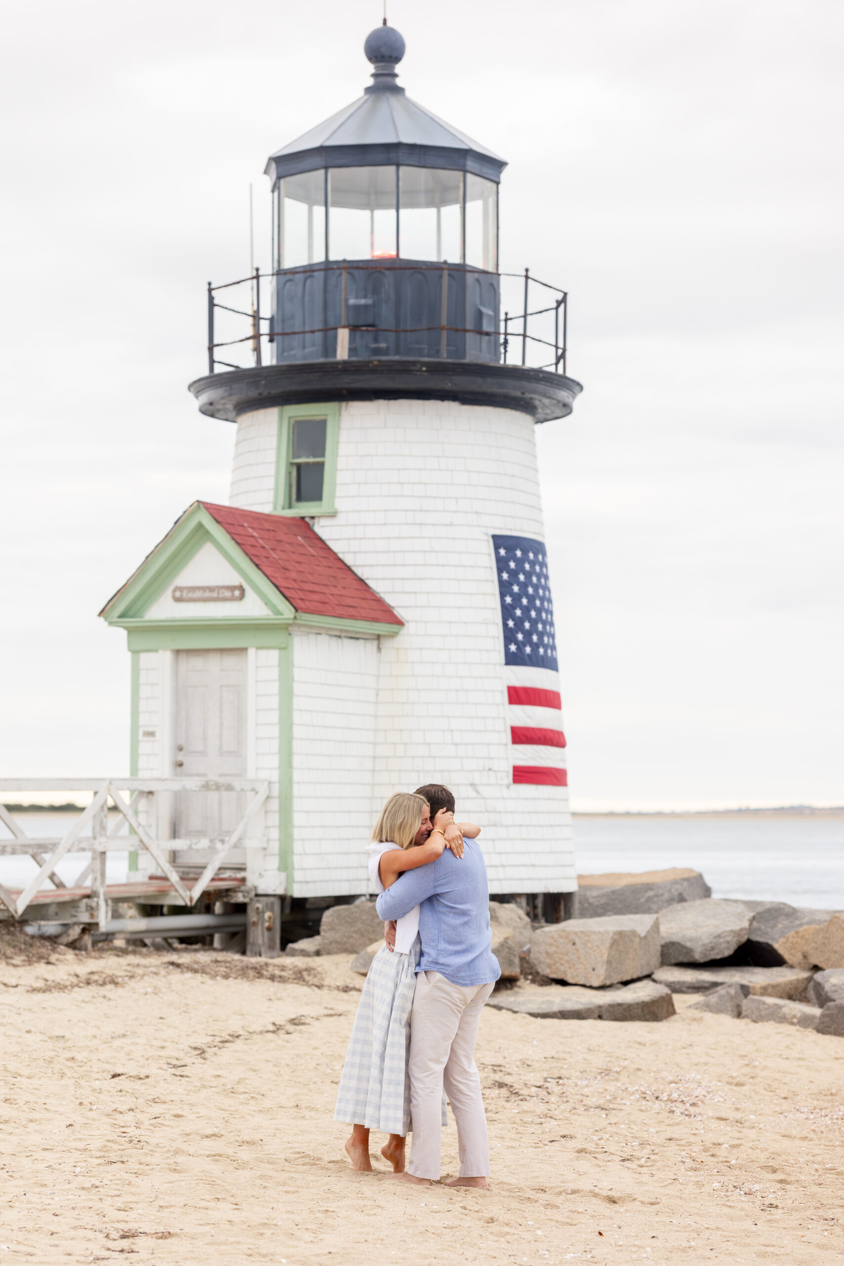 Nantucket Proposal at Brant Point Lighthouse over Memorial Day Weekend with woman and man on beach happily embracing one another.