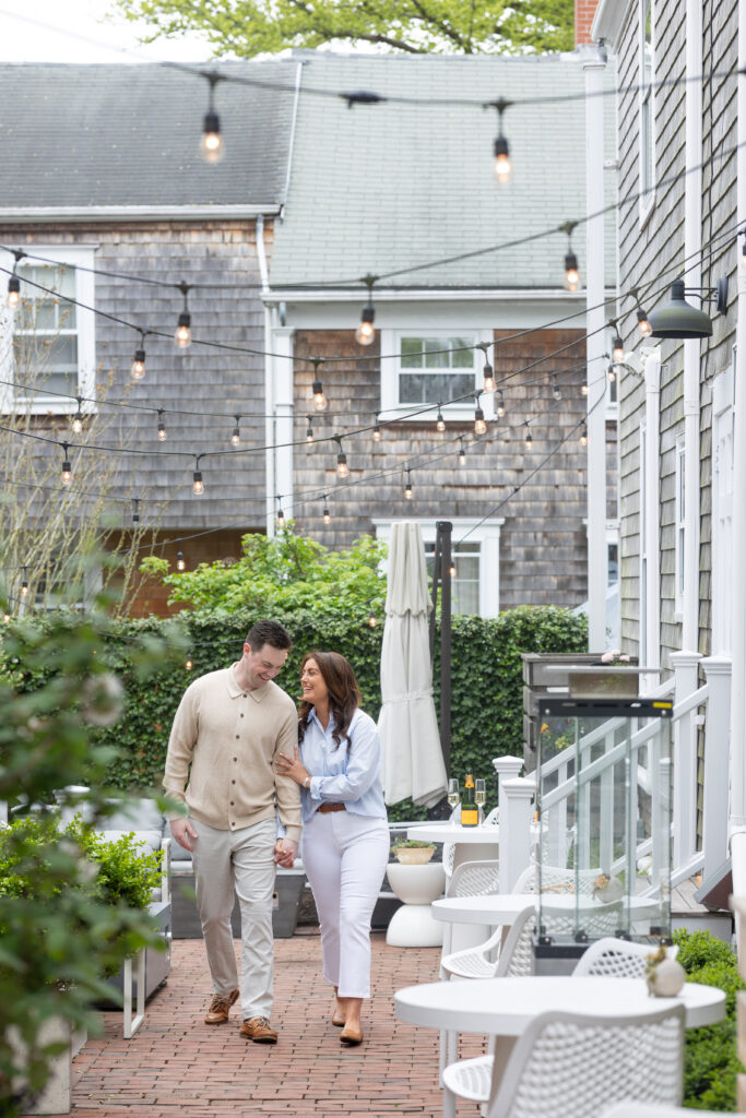 Couple walk under string lights in Nantucket while having engagement pictures taken at Hotel Pippa.