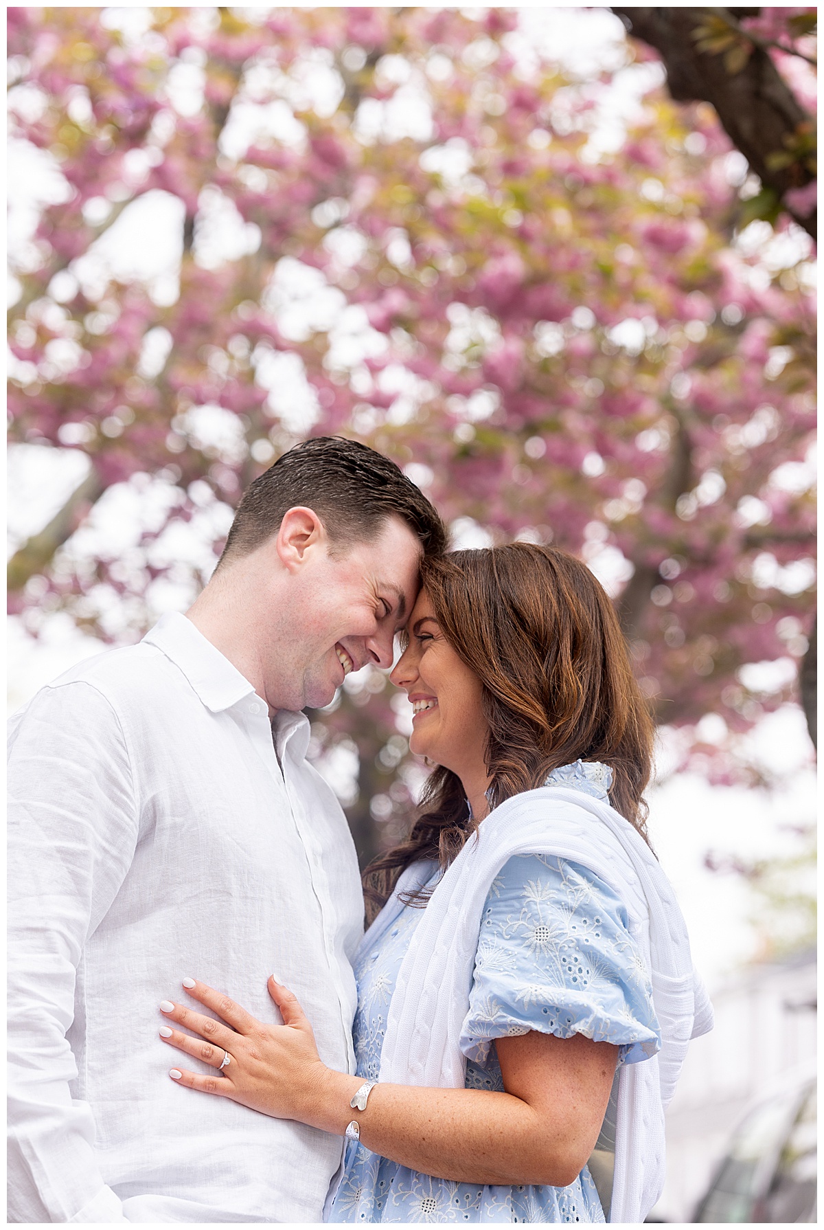 Engagement pictures on Nantucket on a spring day in May. Couple ebraces and touches foreheads under pink blossoms.