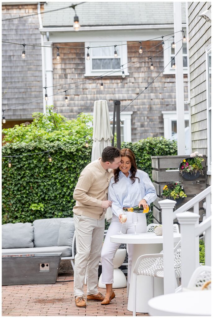 Man kisses women while pouring a glass of champagne during engagement pictures at Hotel Pippa in Nantucket.