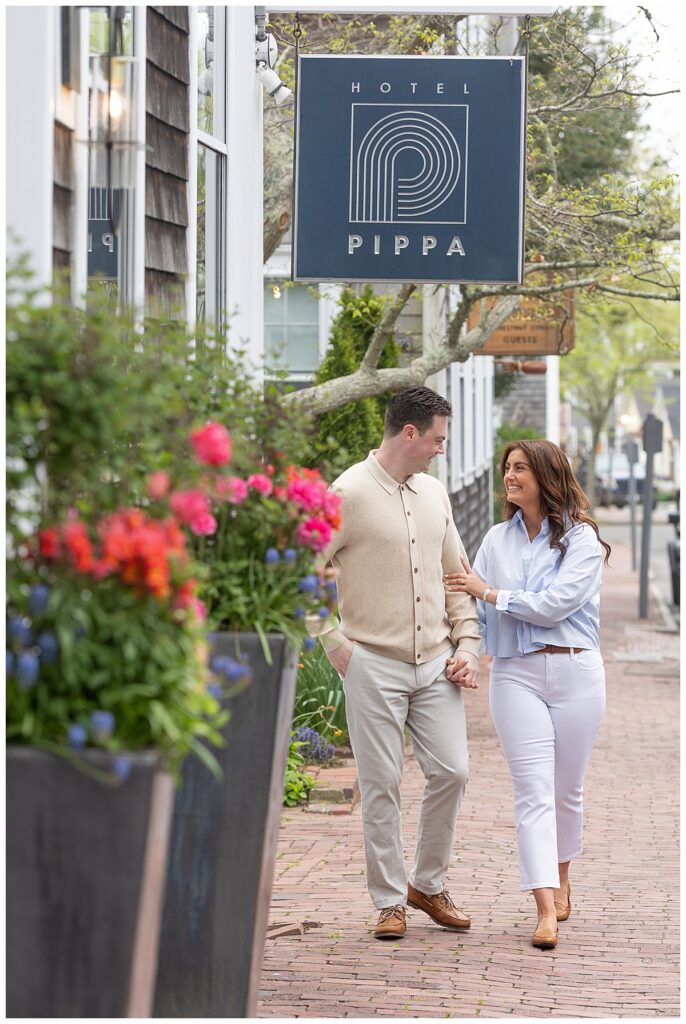 Couple has big smiles under the Hotel Pippa sign while having engagement pictures taken in Nantucket.