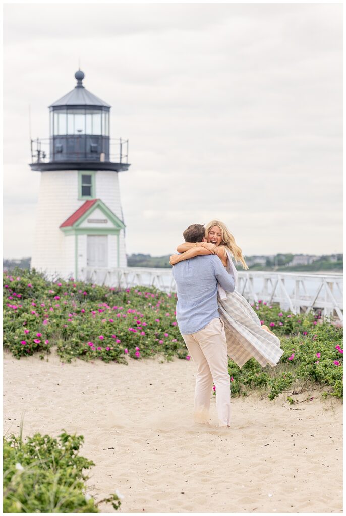Man swings his fiance around smiling and laughing after his Nantucket Proposal at Brant Point Lighthouse in Nantucket.