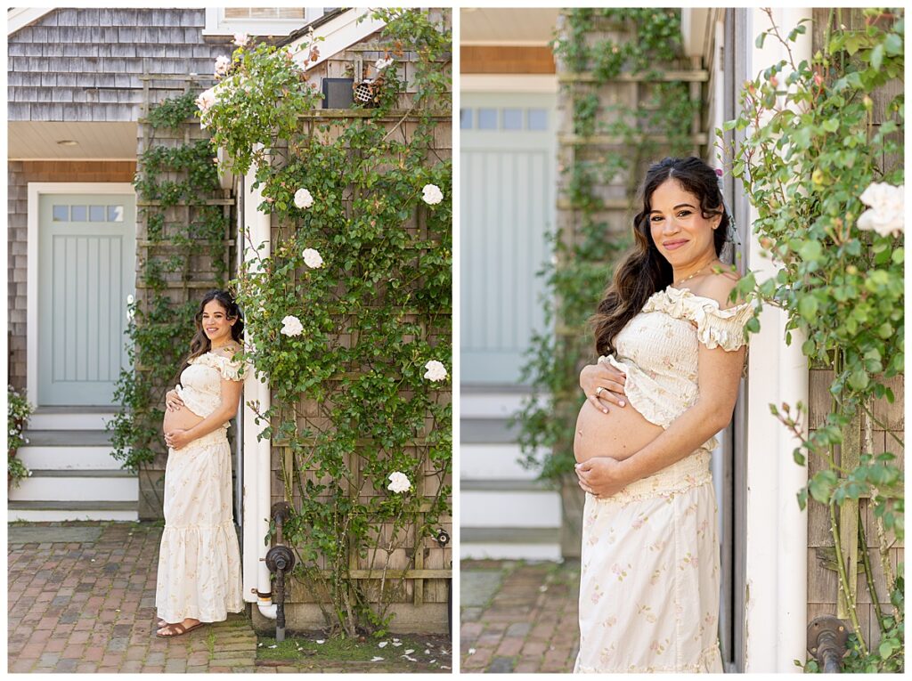 Woman smiles while leaning against a gray shingled building in Nantucket while holding her pregnant belly during Maternity pictures.
