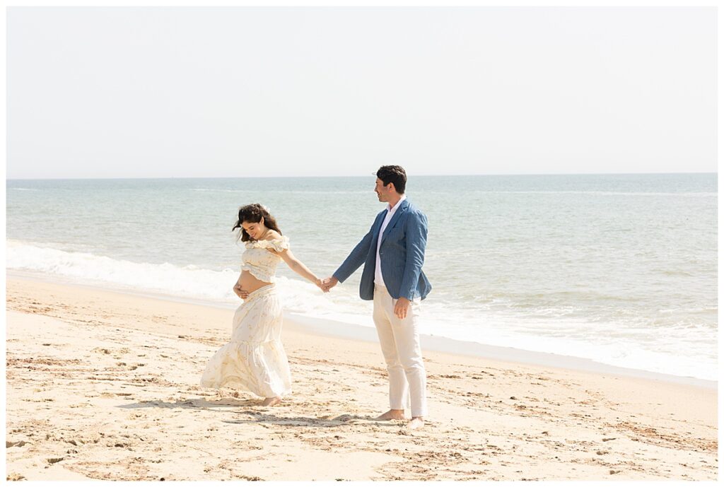 Woman smiles at her pregnant belly at the beach in Sconset, Nantucket while having Maternity pictures taken.