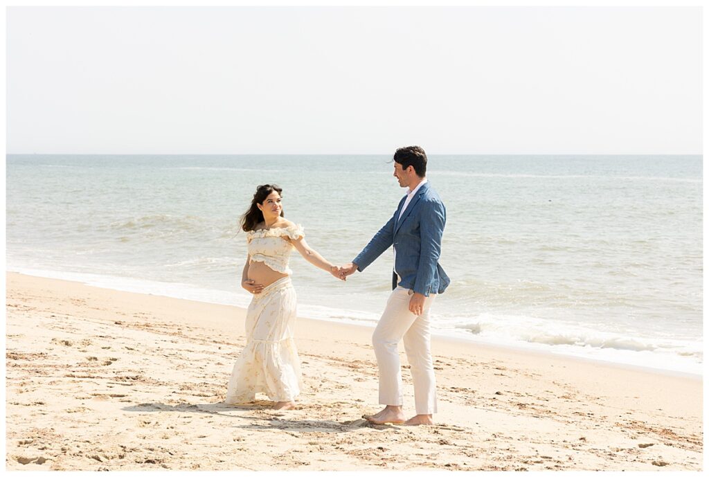 Couple walks hand in hand in Nantucket during Maternity pictures at Sconset beach.