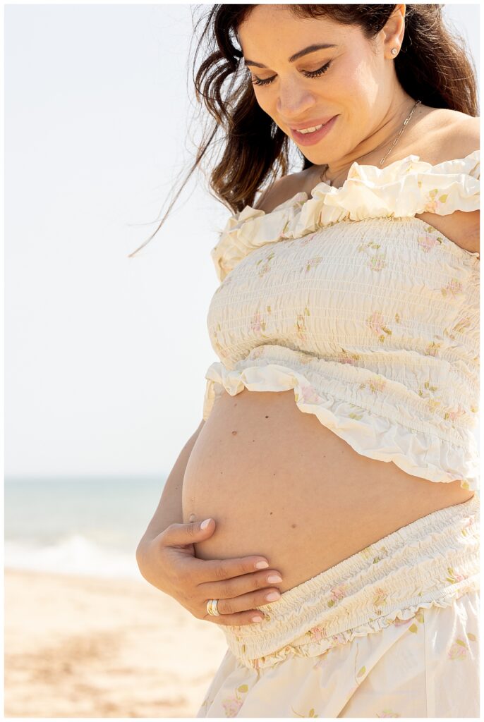 Woman smiles at her pregnant belly in Sconset, Nantucket during Maternity pictures.