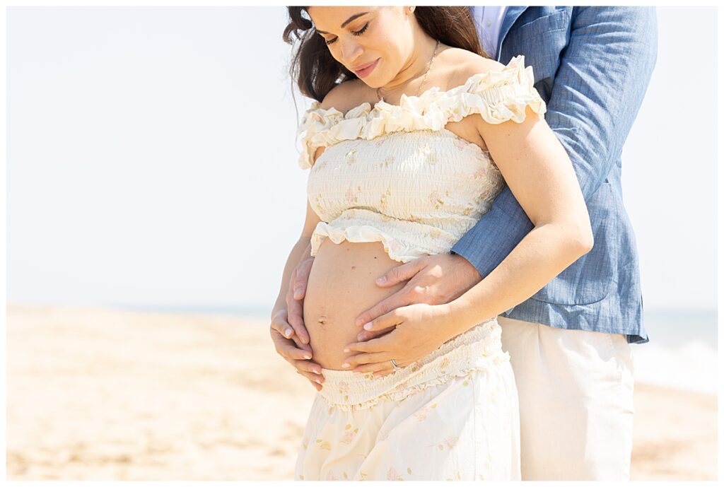 Woman looks down at her belly in Nantucket while at the beach in Sconset during her Maternity pictures.