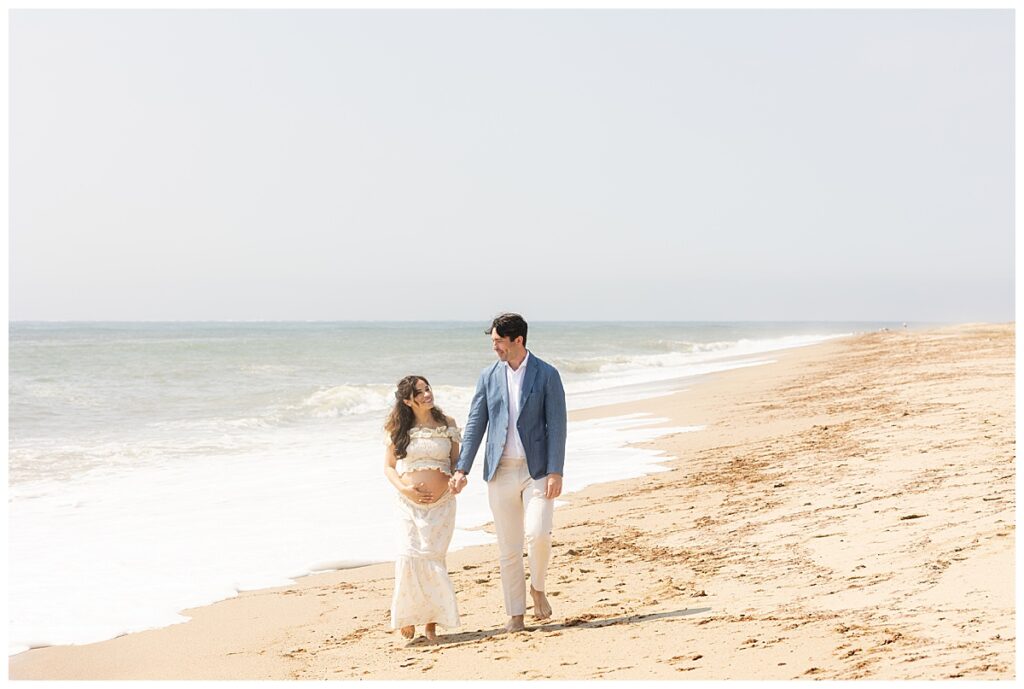 Husband and wife walk along the beach in Nantucket while having Maternity pictures taken at Sconset beach.