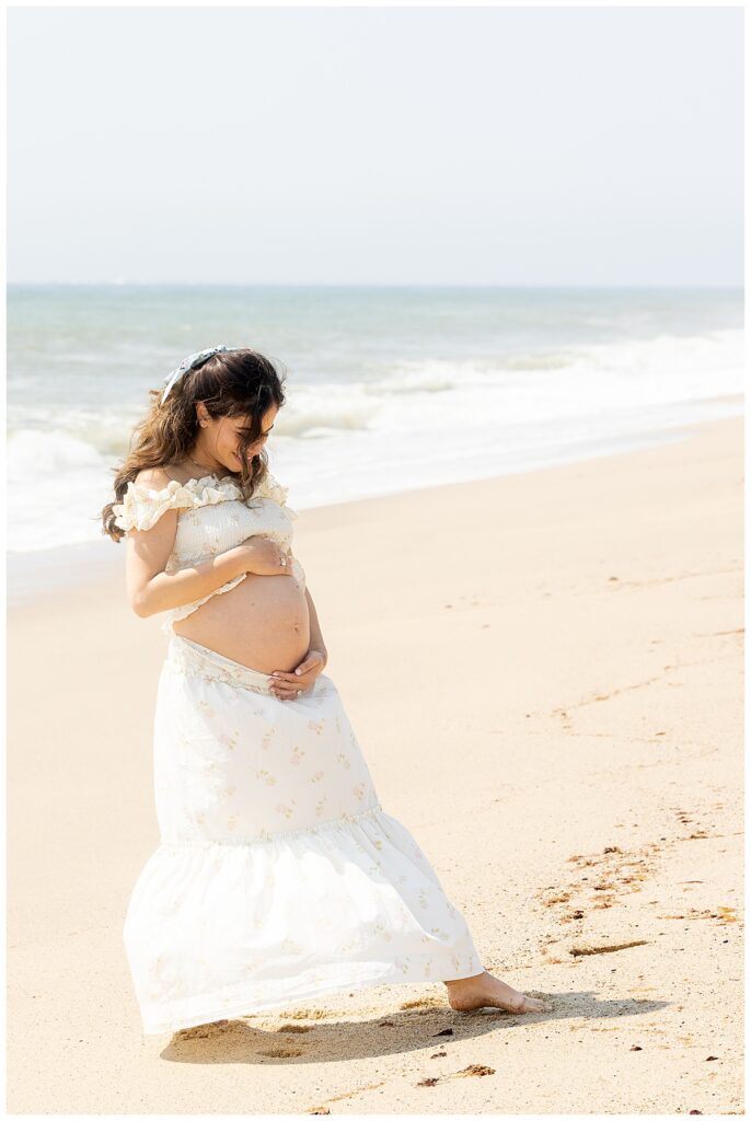 Woman smiles and laughs at her pregnant belly while having Maternity pictures taken in Siasconset, Nantucket beach.