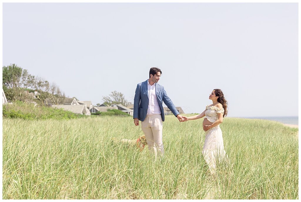 Husband and wife walk in the seagrass in Nantucket along Siasconset beach while having Maternity pictures taken.