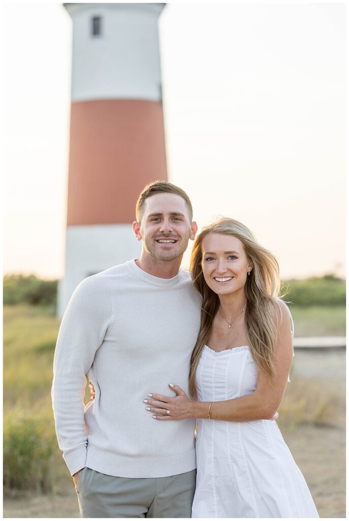 Man wearing a white shirt and woman wearing a white sundress smile after his Nantucket Proposal and Engagment at the Sankaty Head Lighthouse on a warm summer evening in July.