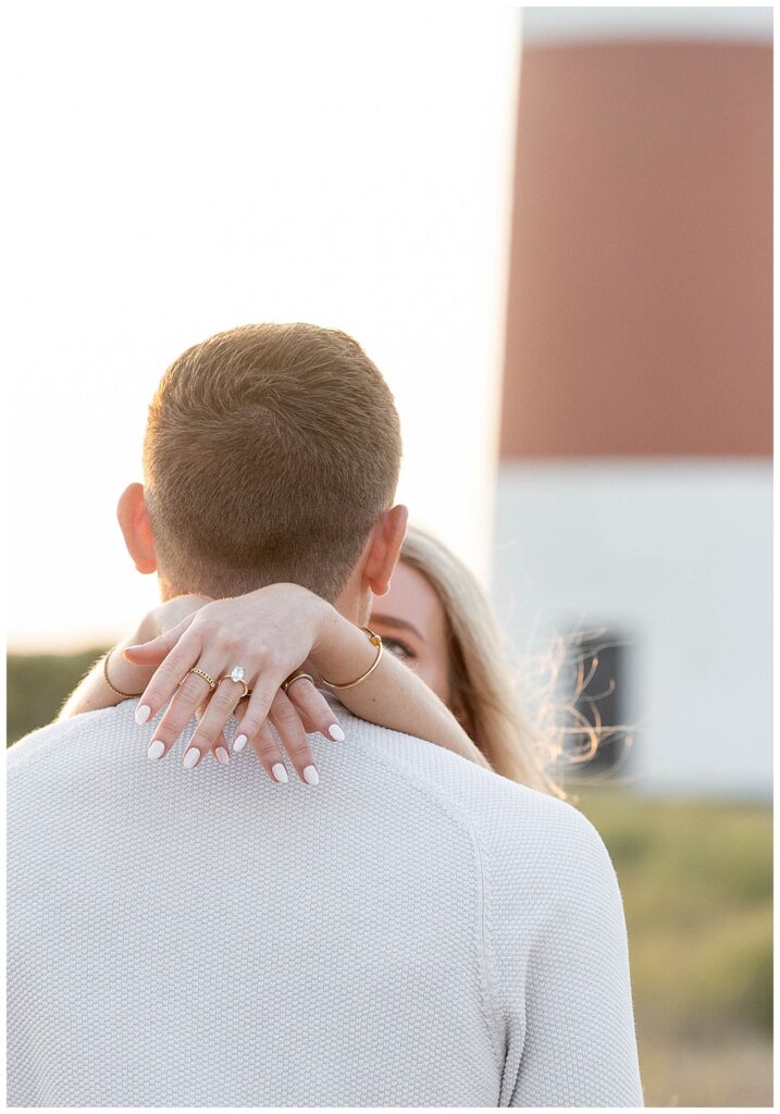 Woman drapes her arms around her new fiance in Nantucket at the Sankaty Head Light after his Nantucket proposal to show off her new diamond ring.