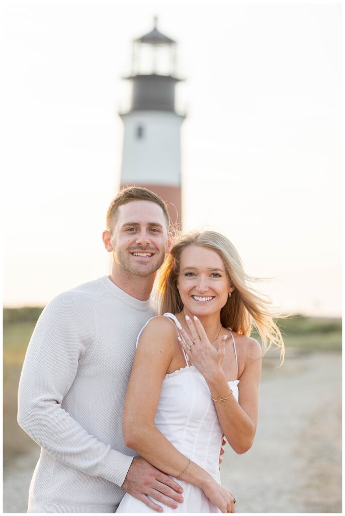 Man and Woman smile after a Nantucket proposal at the Sankaty Head Lighthouse at golden hour on a warm summer evening in July.