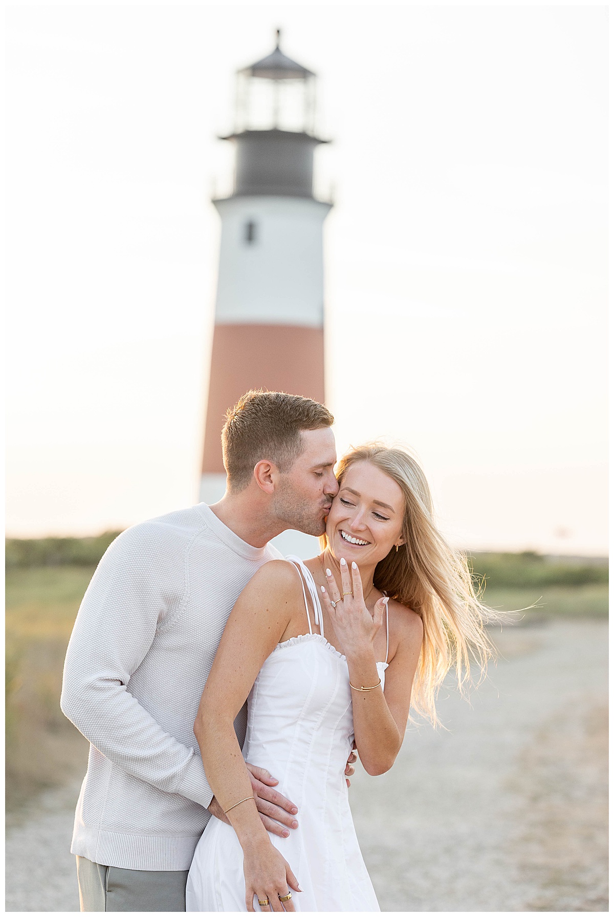 Man kisses woman on the cheek after proposing in Nantucket at the Sankaty Head Lighthouse on a warm July summer evening at golden hour.