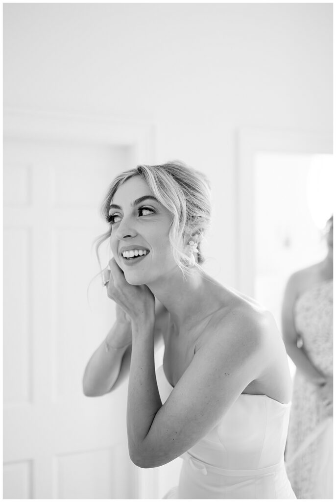 Black and white image of a bride putting on her earrings at her Chatham, Cape Cod wedding.