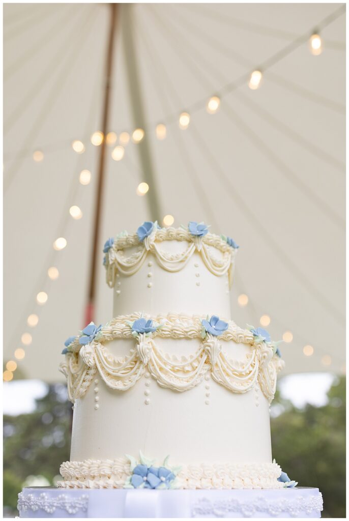 Beautiful cream and baby blue wedding cake under the tent with string lights at a Chatham, Cape Cod wedding.