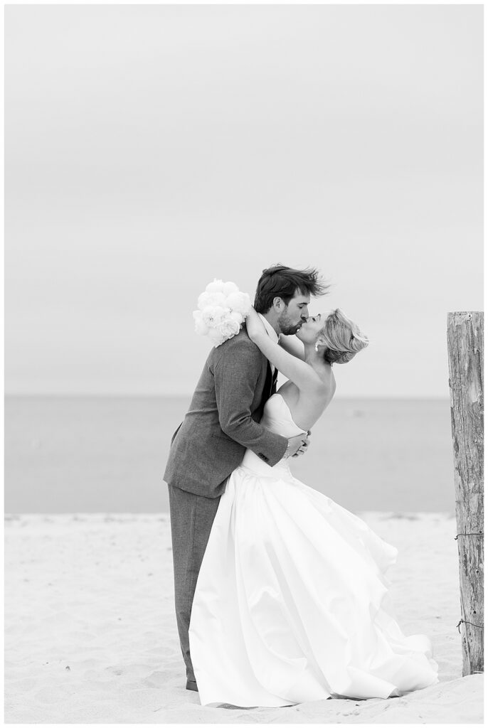 Black and white image of a bride and groom on the beach sharing a kiss at their Chatham, Cape Cod wedding.