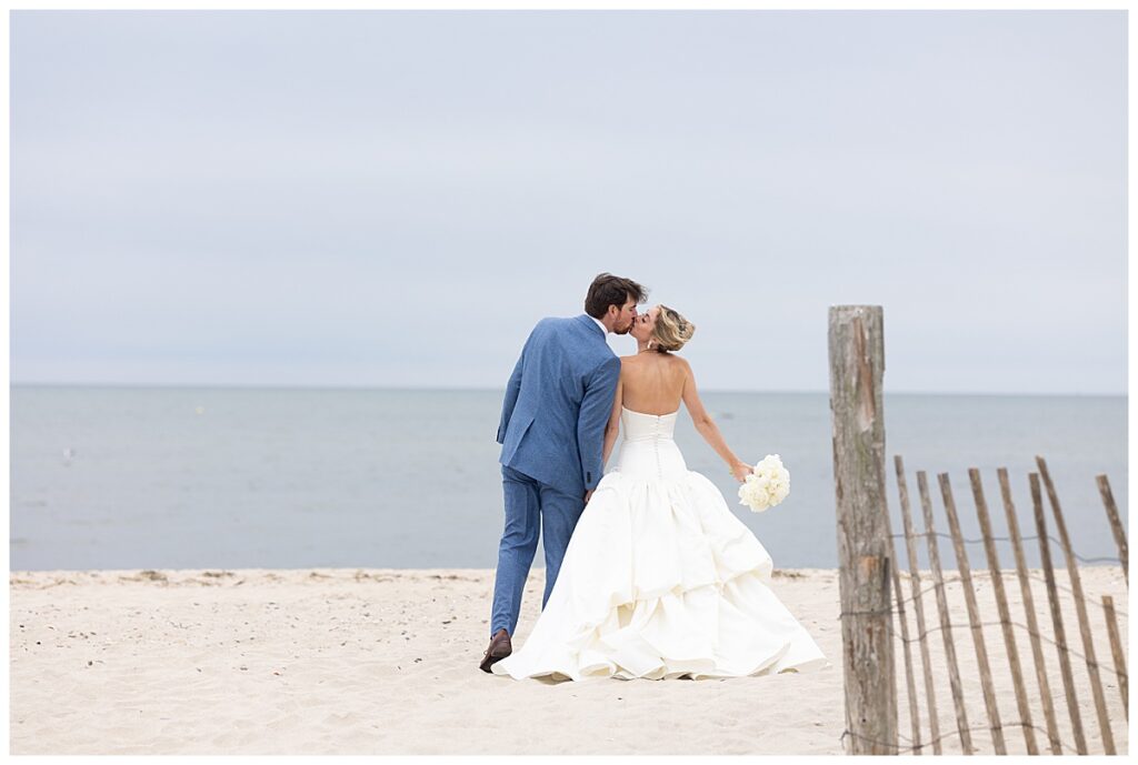 Bride and Groom share a kiss on the beach while holding hands at their Chatham, Cape Cod wedding.