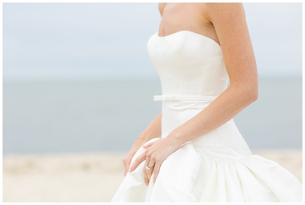 Bride, holds her dress and delicately shows off her ring at the beach at her Chatham, Cape Cod wedding