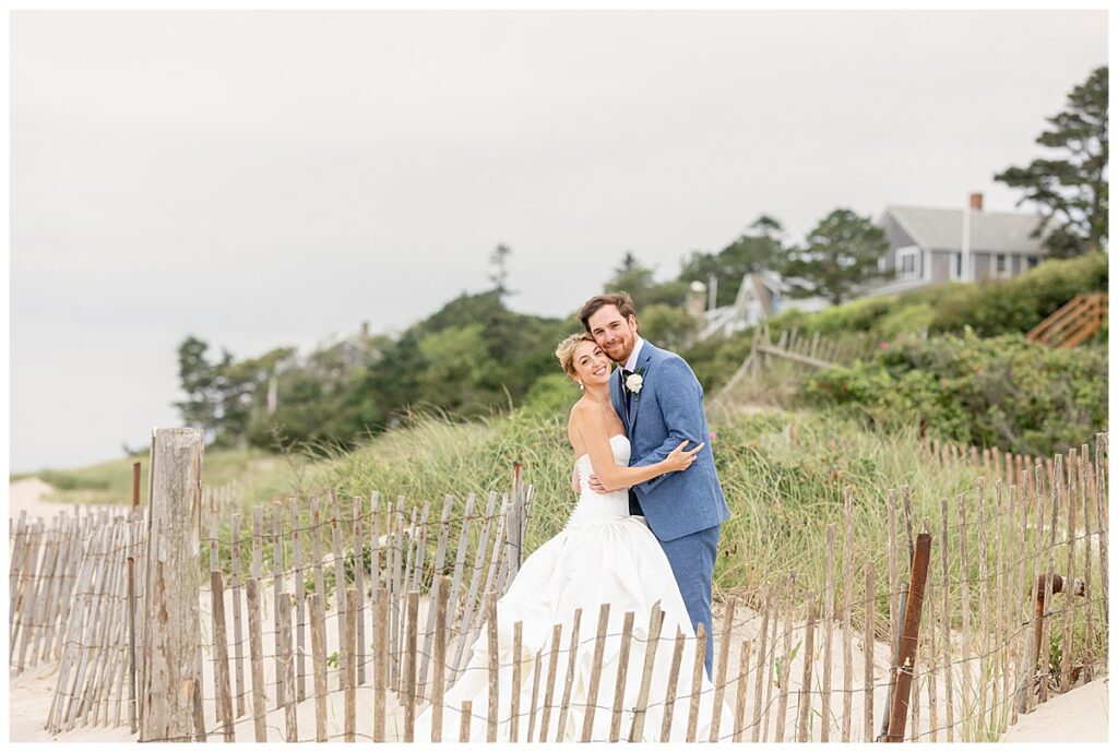 Bride and Groom stand on the beach for some wedding portraits next to the ocean and near the beach fencing at their Chatham, Cape Cod wedding.