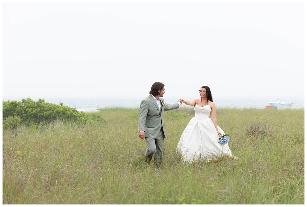 Bride and Groom walk through the seagrass while overlooking the ocean hand and hand at The Wauwinet in Nantucket on their wedding day.