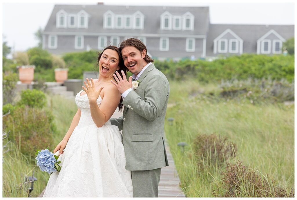 Bride and Groom flash rings and smile in front of The Wauwinet on their wedding day in Nantucket.