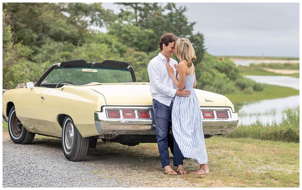 Man and woman touch heads while standing chest to chest as the man leans against a pale yellow classic car.