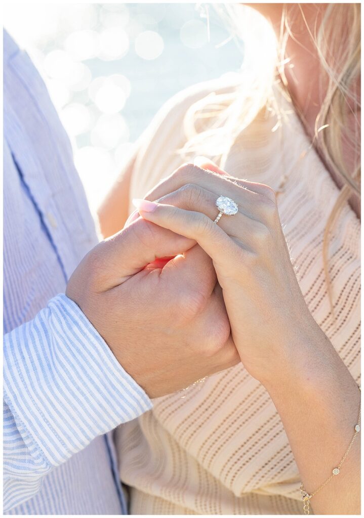 Man holds woman's hand to display her new engagement ring while at Steps Beach over Labor Day weekend after his Nantucket Proposal.
