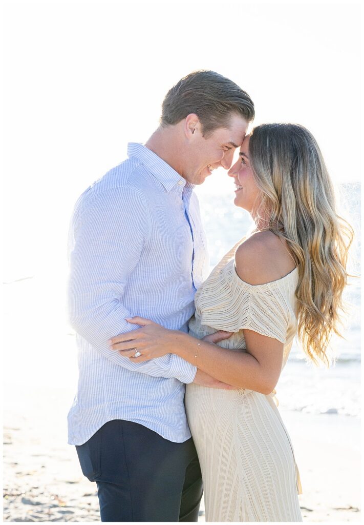 Man and woman touch foreheads and smile at one another after his Nantucket Proposal on Steps Beach over Labor Day weekend.