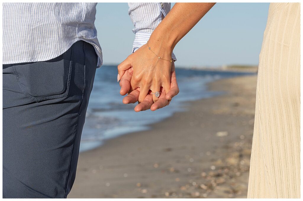 Couple holding hands while walking along Steps Beach in Nantucket, Massachusetts after his proposal.