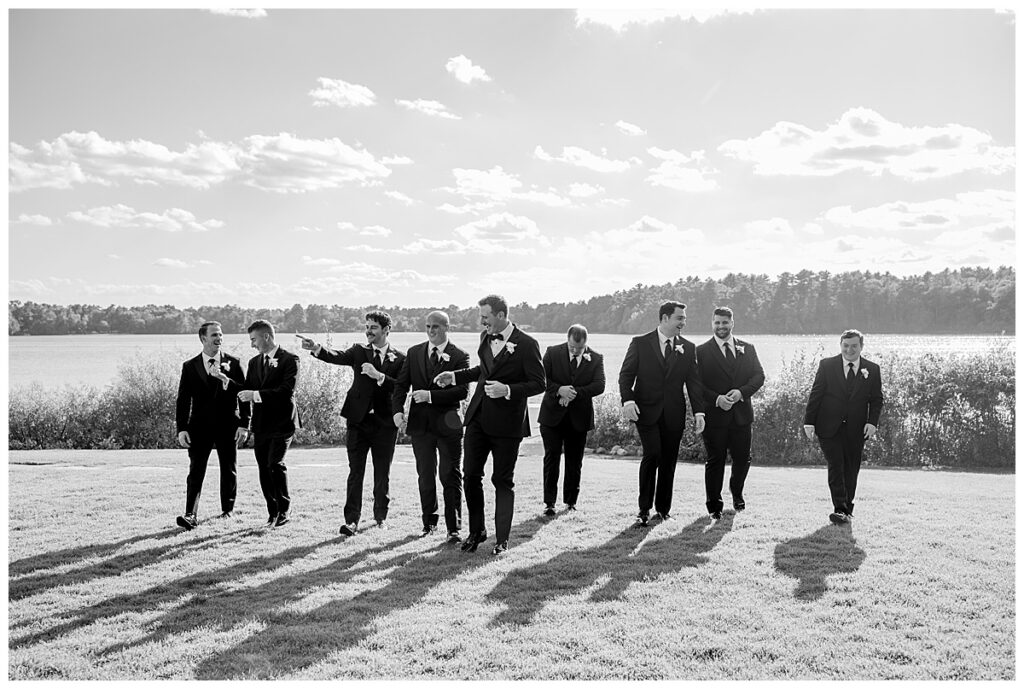 Groom and groomsmen walk along the lawn in black and white photo in Halifax, Cape Cod, Massachusetts at The Lakehouse, a Sapphire Event Group venue.