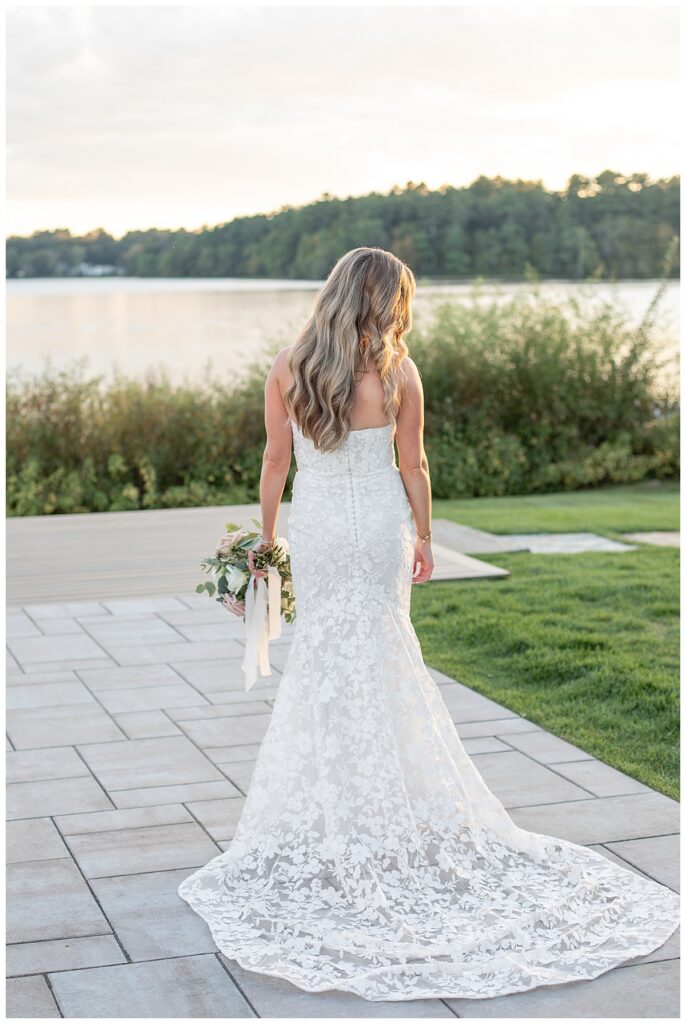 Bride looks over her shoulder with her dress fanned out behind her at her wedding at The Lakehouse, a Sapphire Event Group venue in Halifax, Cape Cod, Massachusetts.