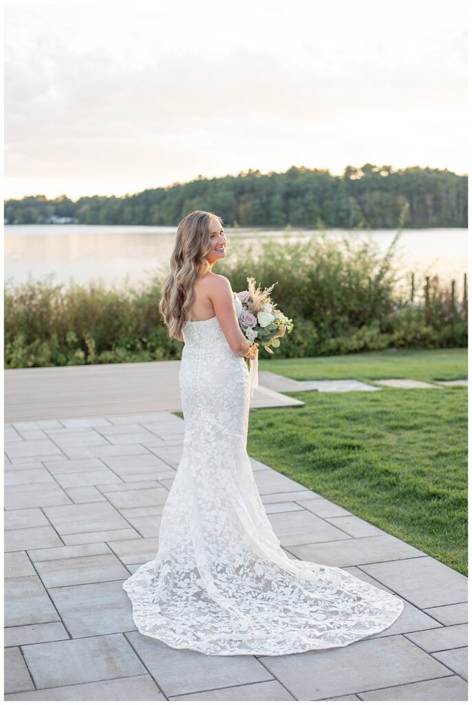 Bride looks over her shoulder with her dress fanned out behind her, at The Lakehouse, a Sapphire Event Group venue in Halifax, Cape Cod, Massachusetts.