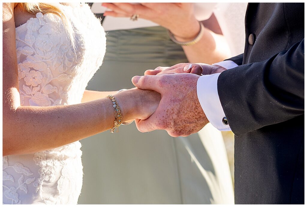 Close up of bride and grooms hands during wedding vows at The Lakehouse, a Sapphire Event Group venue in Halifax, Cape Cod, Massachusetts.