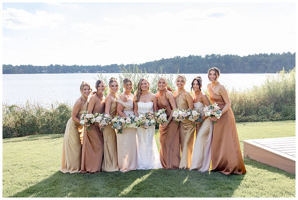 Bride and Bridesmaids on the lawn in front of the water at The Lakehouse, a Sapphire Event Group, in Halifax, Cape Cod, Massachusetts.