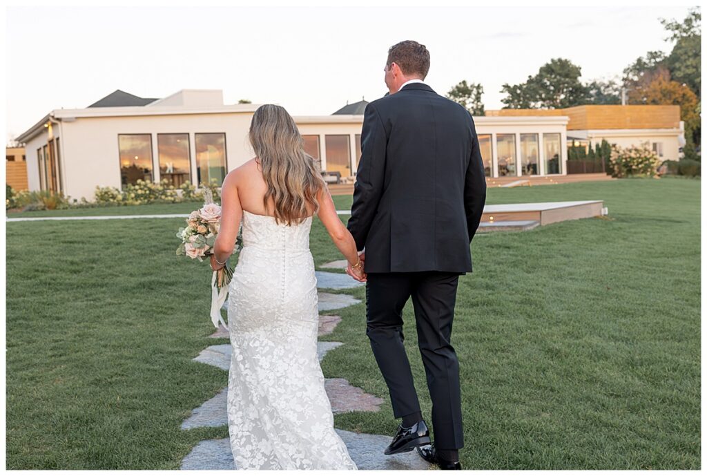 Bride and groom walk towards The Lakehouse, a Sapphire Event Group venue in Halifax, Cape Cod, Massachusetts at sunset.