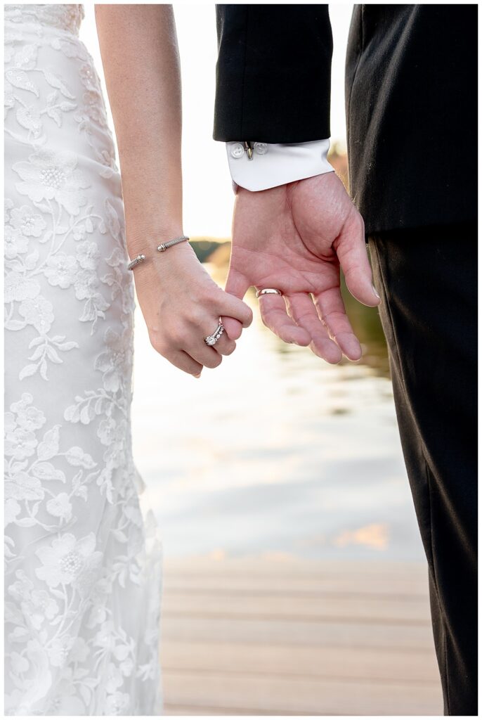 Bride and Groom lock pinkie fingers while standing on the dock of The Lakehouse, a Sapphire Event Group venue at sunset on their wedding day.