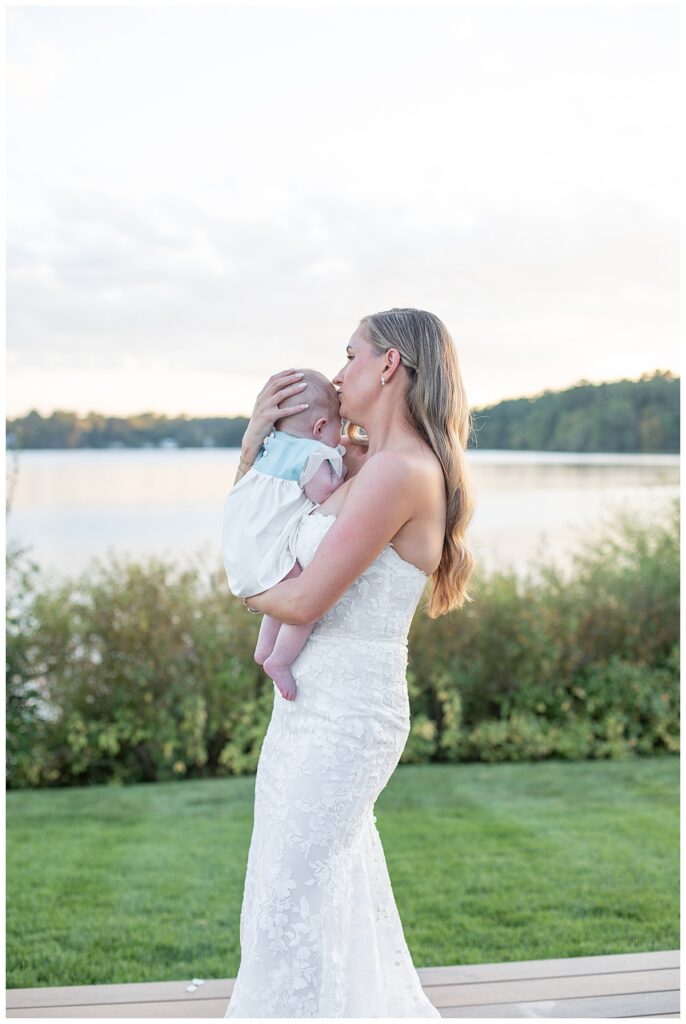 Bride kisses baby daughter at her wedding in Halifax, Cape Cod, Massachusetts on a sunny evening in September over looking the water.