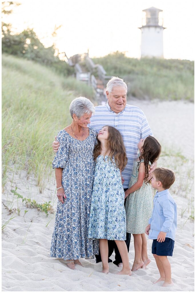Grandparents smile at their 3 grandkids at Chatham Lighthouse Beach at sunset in Chatham, Cape Cod, Massachusetts.