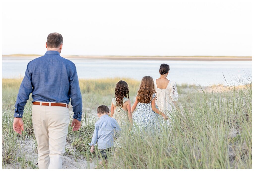 Family of five walk toward the beach in a line at sunset at Chatham Lighthouse Beach in Chatham, Cape Cod, Massachusetts.