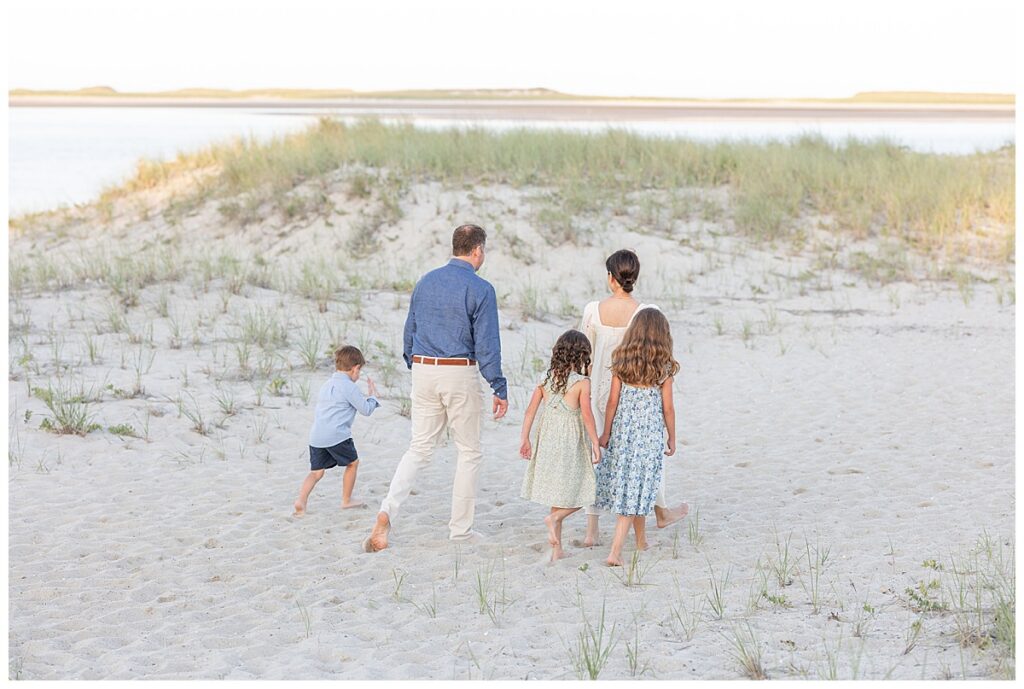 Family walks facing the ocean as they walk towards the water at sunset at Chatham Lighthouse Beach in Chatham, Cape Cod, Massachusetts.
