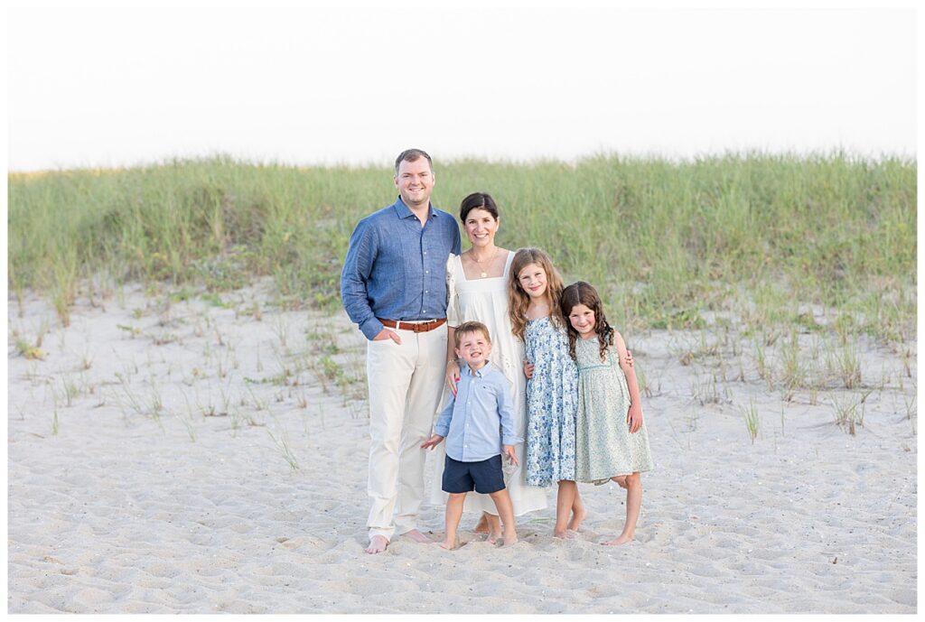 Family of five standing in the sand in front of a sand dune covered in seagrass at sunset at Chatham Lighthouse Beach in Chatham, Cape Cod, Massachusetts.