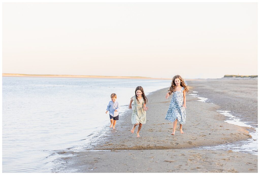 Kids run along the beach laughing with each other at sunset at Chatham Lighthouse Beach in Chatham, Cape Cod, Massachusetts.