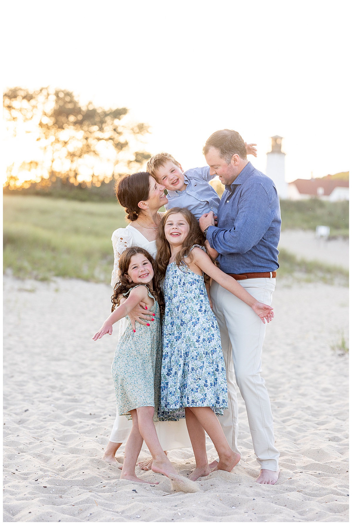 Family smiles and laughs while they embrace each other in front of the Chatham Lighthouse at Chatham Lighthouse beach in Chatham, Cape Cod, Massachusetts.