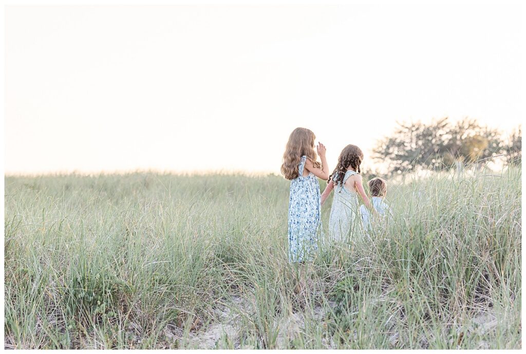 Kids walk in a line up a sand dune hill in the seagrass at sunset at Chatham Lighthouse beach in Chatham, Cape Cod, Massachusetts.